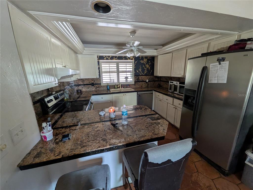 A kitchen features white cabinets, dark granite countertops, a stainless steel refrigerator, and tiled flooring — 7167 COLUMBIA CIRCLE, FORT MYERS, FL