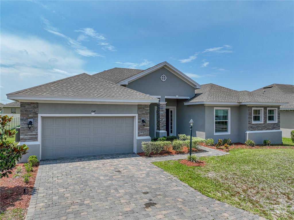 A single-story house with a gray stucco exterior, stone accents, and a paved driveway — 1547 CORDGRASS WAY, LAKELAND, FL
