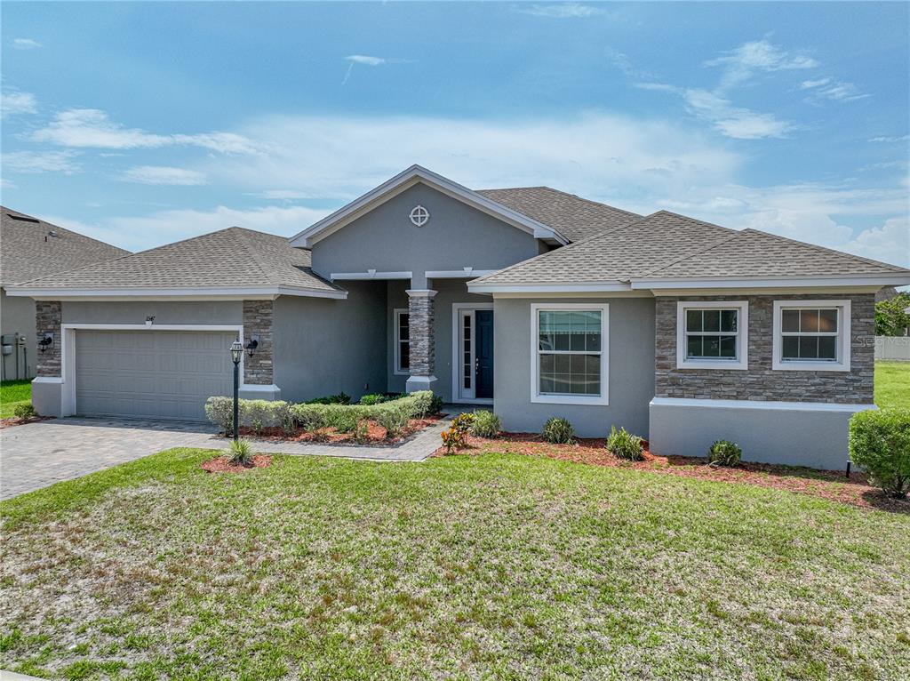 A single-story house features a gray stucco exterior, stone accents, and a two-car garage — 1547 CORDGRASS WAY, LAKELAND, FL