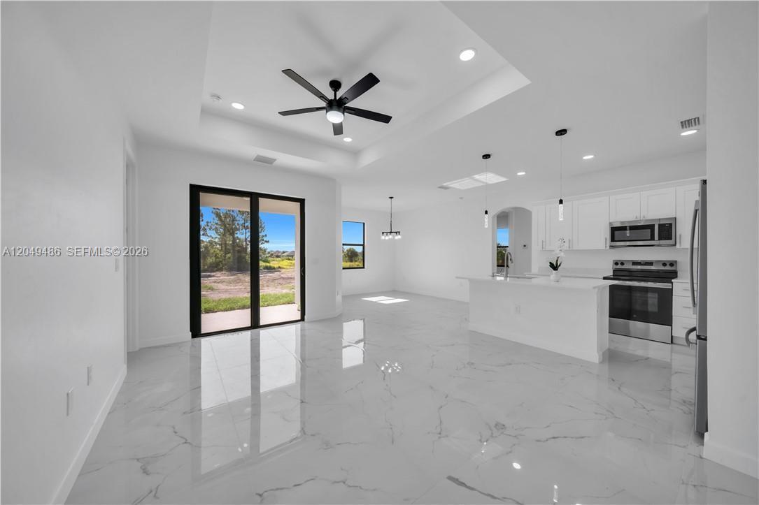 A bright, open-concept kitchen and living area features white cabinetry, stainless appliances, and marble-look flooring — 800 Pine Ave, Lehigh Acres FL 33972, LEHIGH ACRES, FL