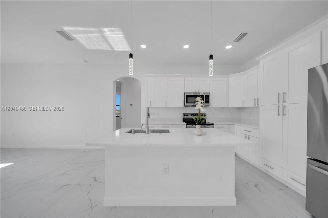 A modern white kitchen features a central island, stainless steel appliances, and marble-style flooring — 800 Pine Ave, Lehigh Acres FL 33972, LEHIGH ACRES, FL
