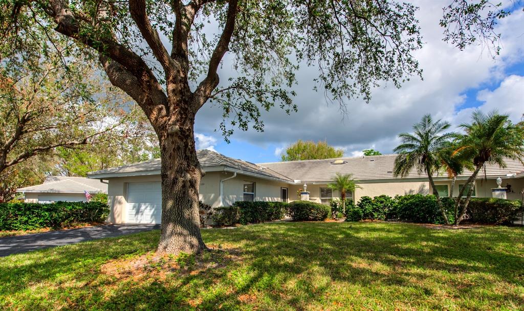 A single-story house with a white garage, large oak tree, and palm trees in front — 130 SOUTHAMPTON PLACE UNIT 360, VENICE, FL
