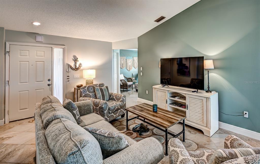 A living room features a blue accent wall, a television console, and patterned seating furniture — 130 SOUTHAMPTON PLACE UNIT 360, VENICE, FL