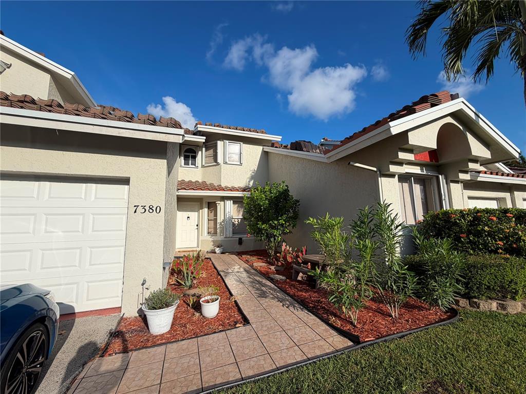 The exterior of a two-story house features a tiled walkway, garage, and landscaped front yard — 7380 PINEWALK DRIVE S UNIT 37-8, MARGATE, FL