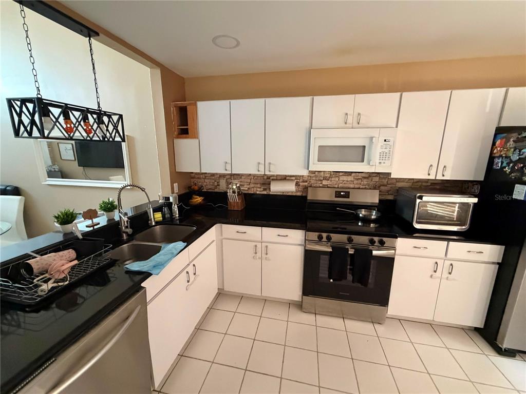 A kitchen features white cabinets, black countertops, stainless steel appliances, and a tiled floor — 7380 PINEWALK DRIVE S UNIT 37-8, MARGATE, FL