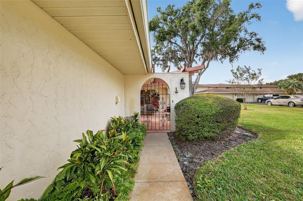 A concrete walkway leads to an arched gated entrance of a house with stucco walls — 100 S TREMAIN STREET UNIT F1, MOUNT DORA, FL