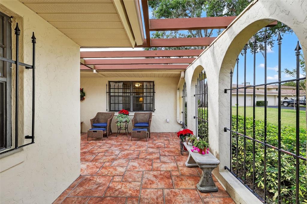 A covered patio features a tiled floor, wicker chairs, and a decorative metal security fence — 100 S TREMAIN STREET UNIT F1, MOUNT DORA, FL