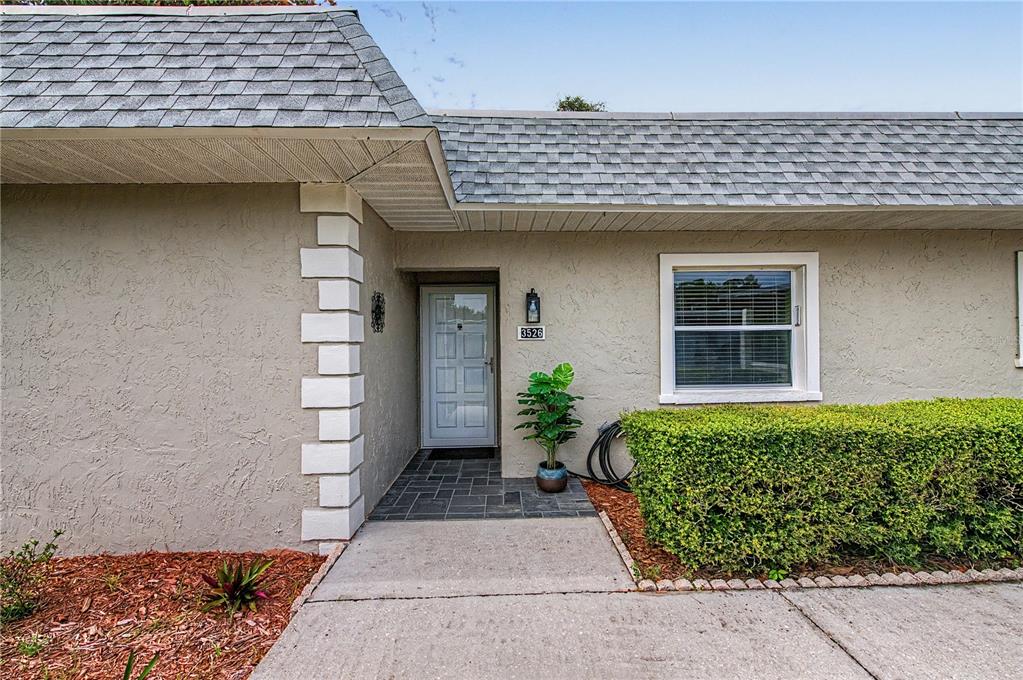 The exterior of a house features a gray stucco facade, a shingled roof, and landscaping — 3526 TEESIDE DRIVE, NEW PORT RICHEY, FL
