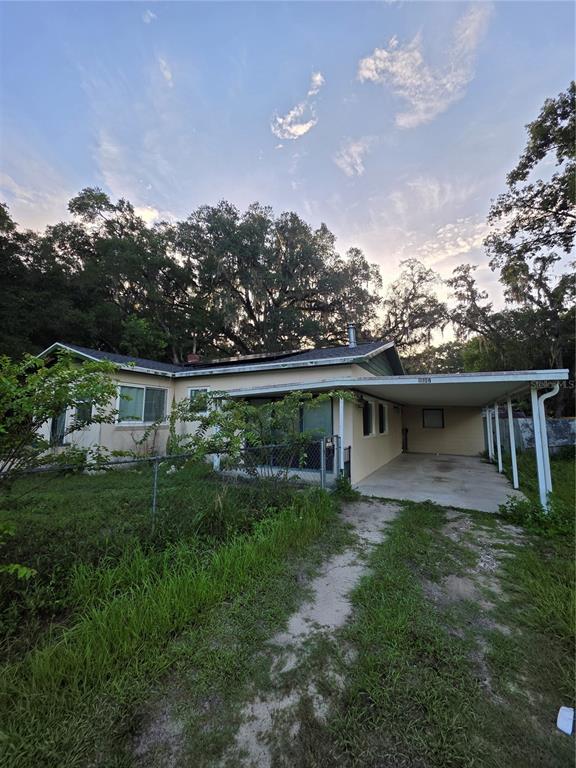 A single-story house with a carport, chain-link fence, and large trees in the background — 11647 SE 60TH AVENUE, BELLEVIEW, FL