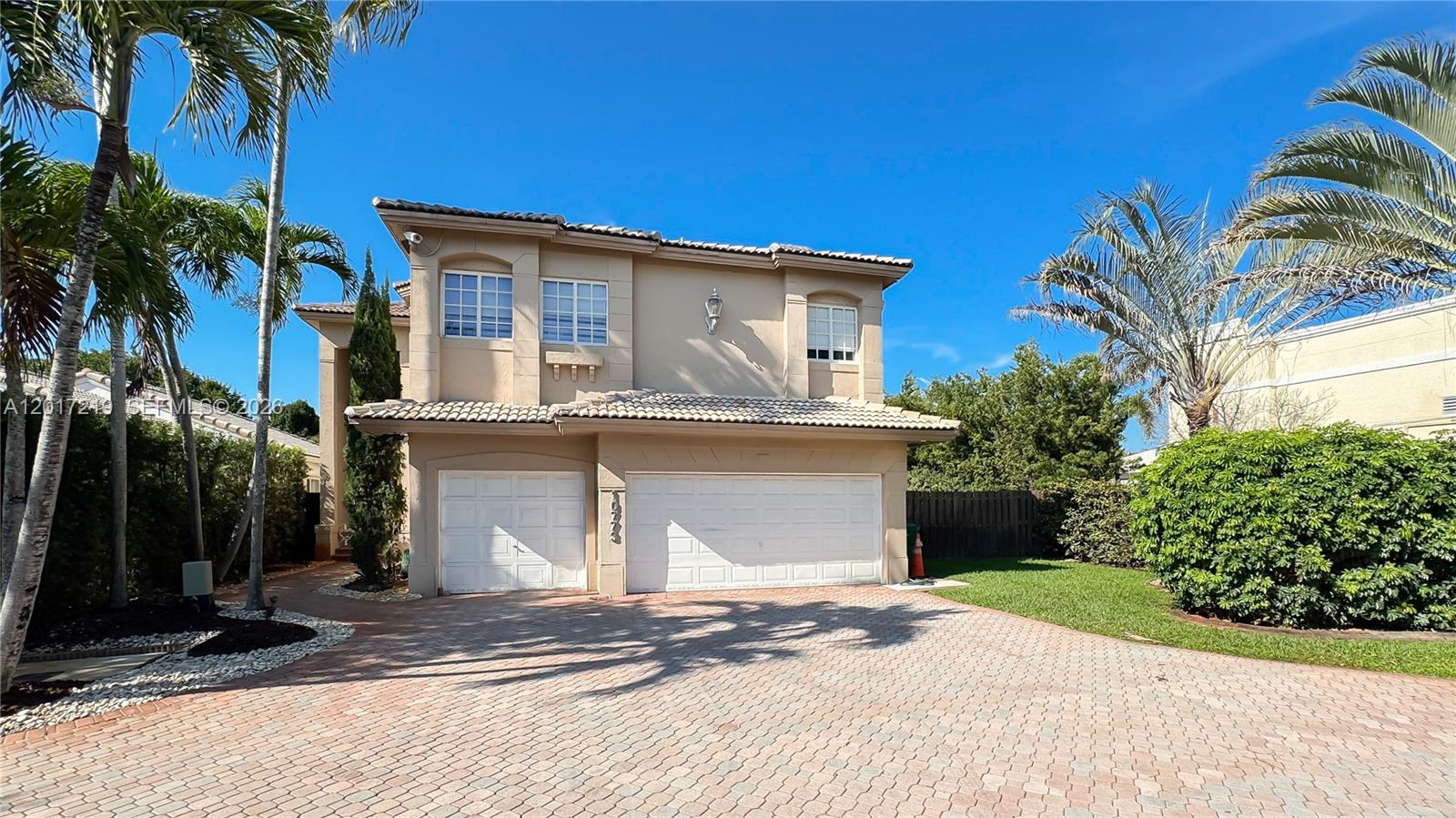 A two-story beige house features a paved driveway, two garage doors, and surrounding palm trees — 10773 NW 73rd Ter, Doral FL 33178, DORAL, FL