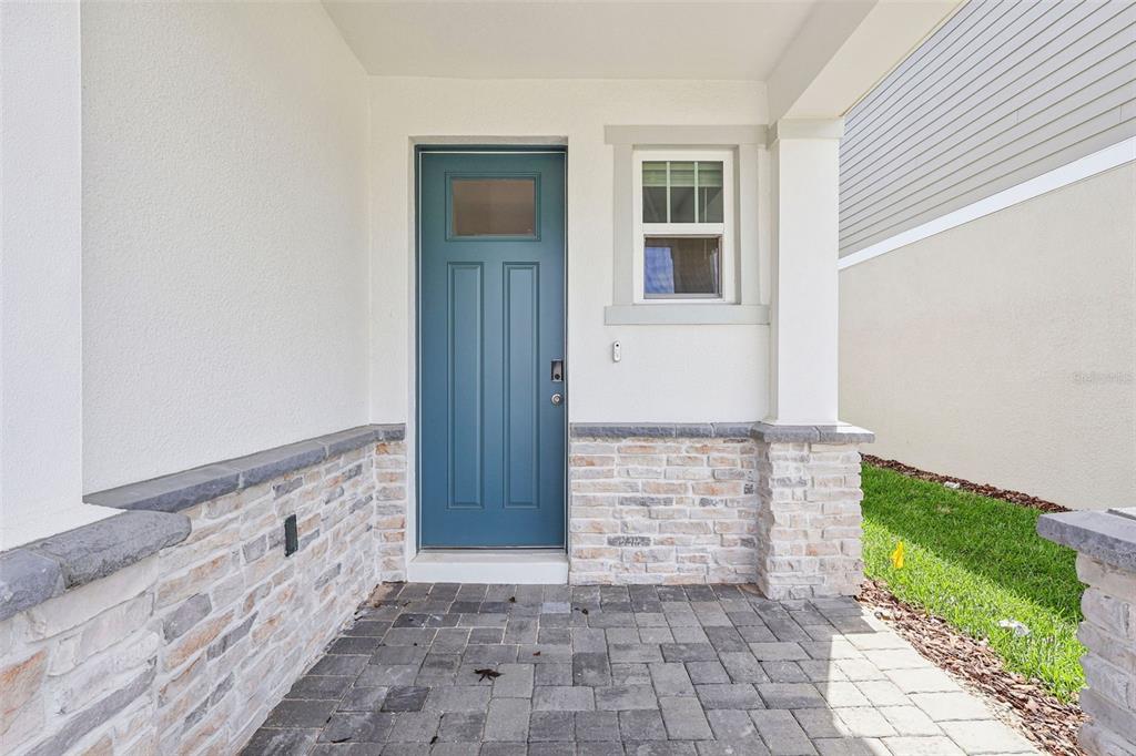 A blue front door with a window sits on a stone-accented porch with pavers — 2277 HEN ROAD, MINNEOLA, FL