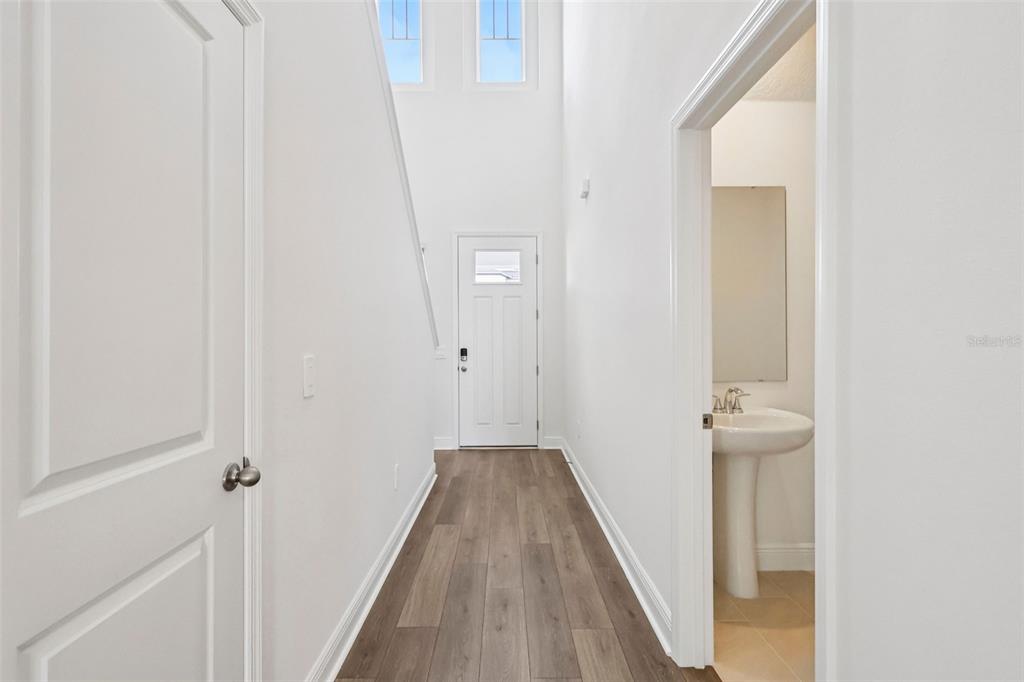 A bright entryway features wood-look flooring, a white front door, and an adjacent half bathroom — 2277 HEN ROAD, MINNEOLA, FL