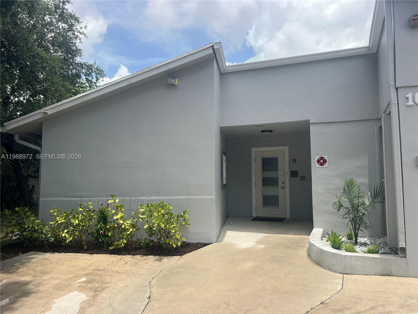 The exterior of a gray building features a recessed entrance, a concrete walkway, and landscaping — 1633 NW 4th St, Boca Raton FL 33486, BOCA RATON, FL