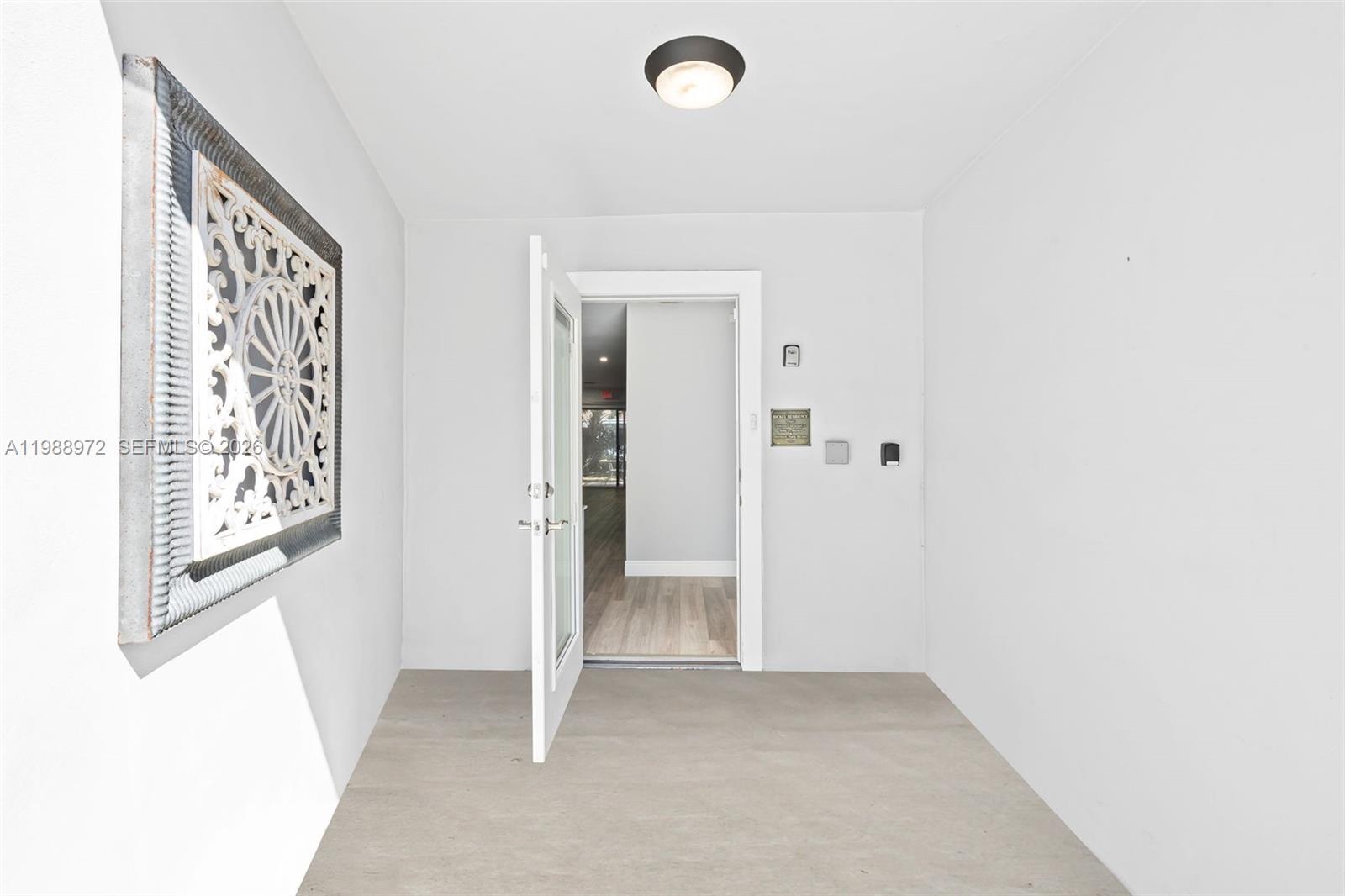 An open white door leads from a covered entryway into a room with wood flooring — 1633 NW 4th St, Boca Raton FL 33486, BOCA RATON, FL