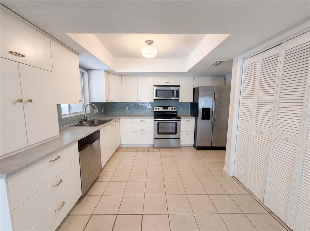 A kitchen features white cabinetry, stainless steel appliances, a tiled backsplash, and light-colored floor tiles — 2534 VICTARRA CIRCLE, LUTZ, FL
