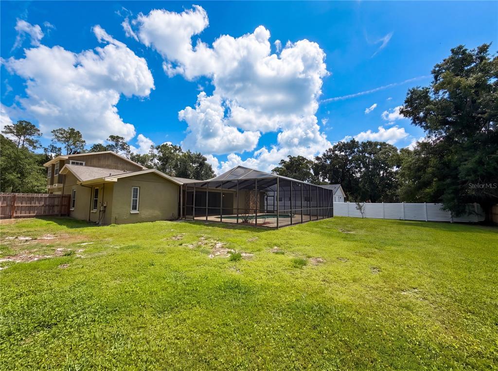 A backyard view of a house with a screened-in pool enclosure and a wooden fence — 2534 VICTARRA CIRCLE, LUTZ, FL