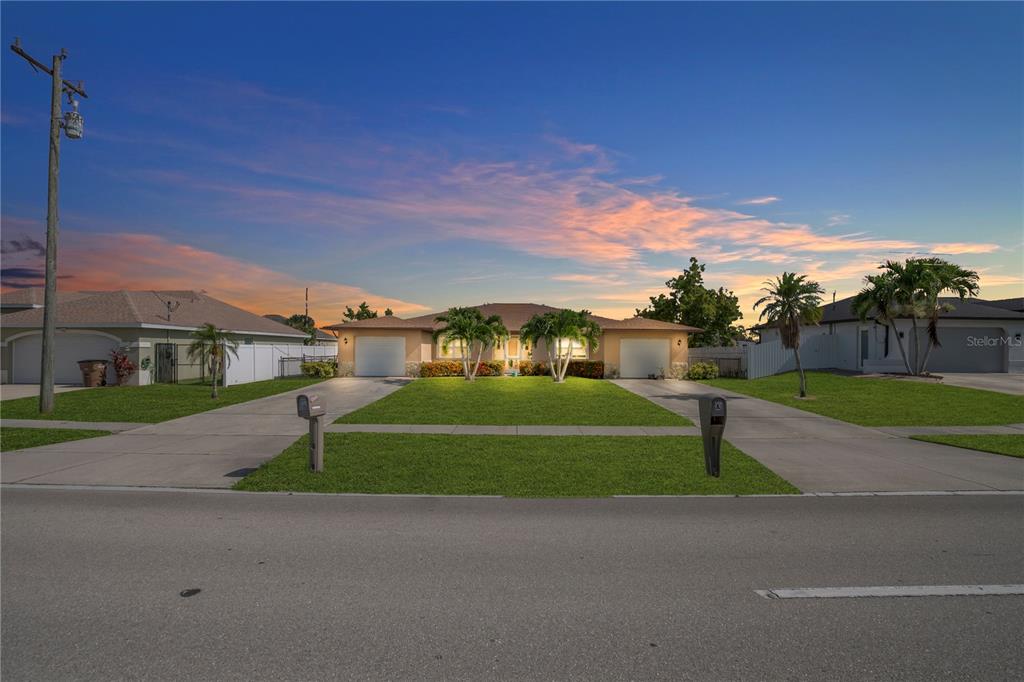 A single-story house with two garages and a front lawn under a sunset sky — 836 SW TRAFALGAR PKWY, CAPE CORAL, FL