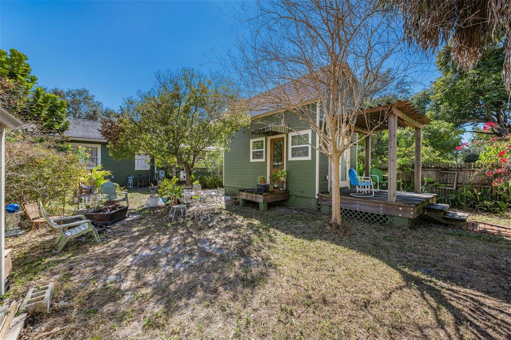 A green cottage with a wooden deck and pergola sits in a grassy backyard — 3411 W BAY AVENUE, TAMPA, FL