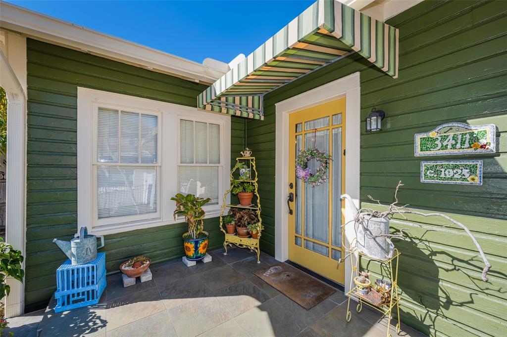 A yellow front door with a striped awning sits on a porch with green siding — 3411 W BAY AVENUE, TAMPA, FL