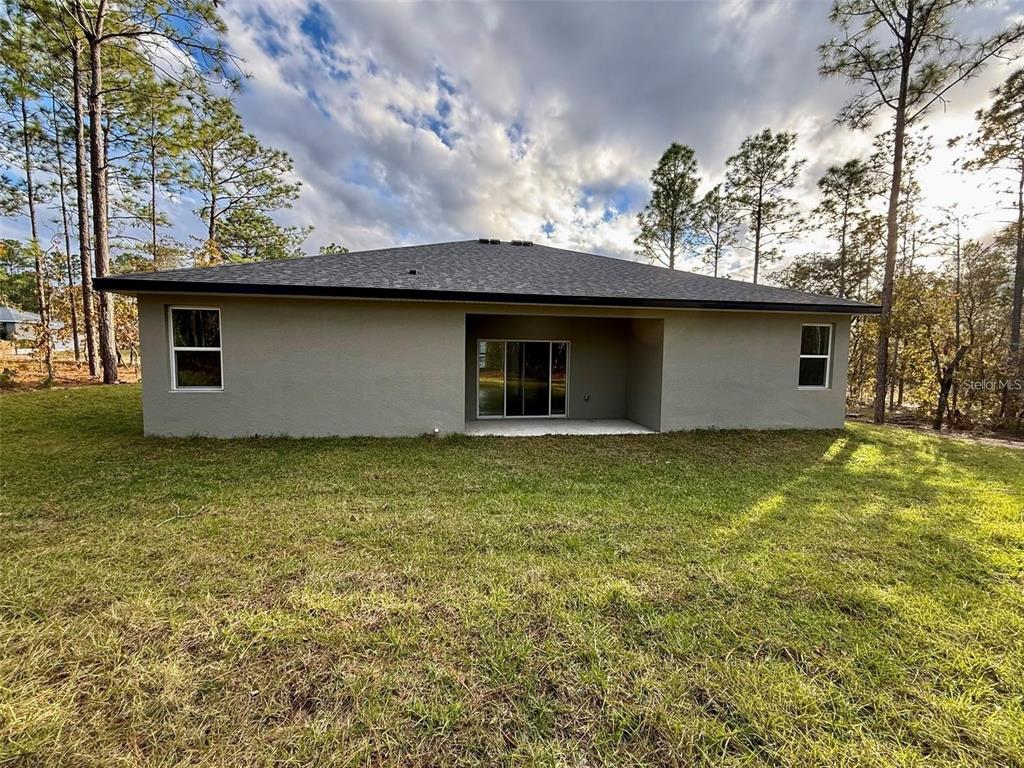 The rear exterior of a single-story house with a covered patio and a grassy yard — 2744 W REDGATE DRIVE, DUNNELLON, FL