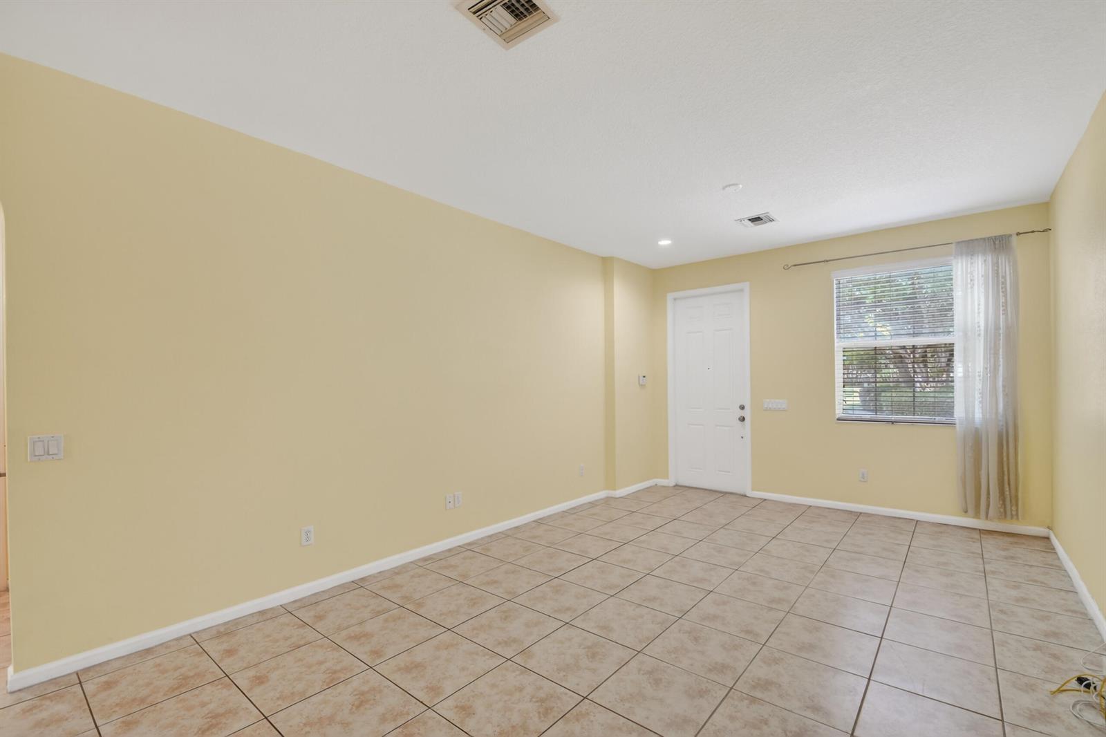 An empty room with light yellow walls, beige tile flooring, a white door, and window — 7480 Sarentino Lane, Boynton Beach FL 33437, BOYNTON BEACH, FL