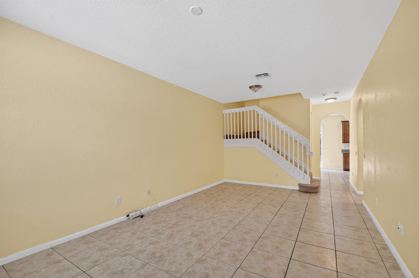 An empty room with yellow walls, tile flooring, and a white staircase leading upstairs — 7480 Sarentino Lane, Boynton Beach FL 33437, BOYNTON BEACH, FL