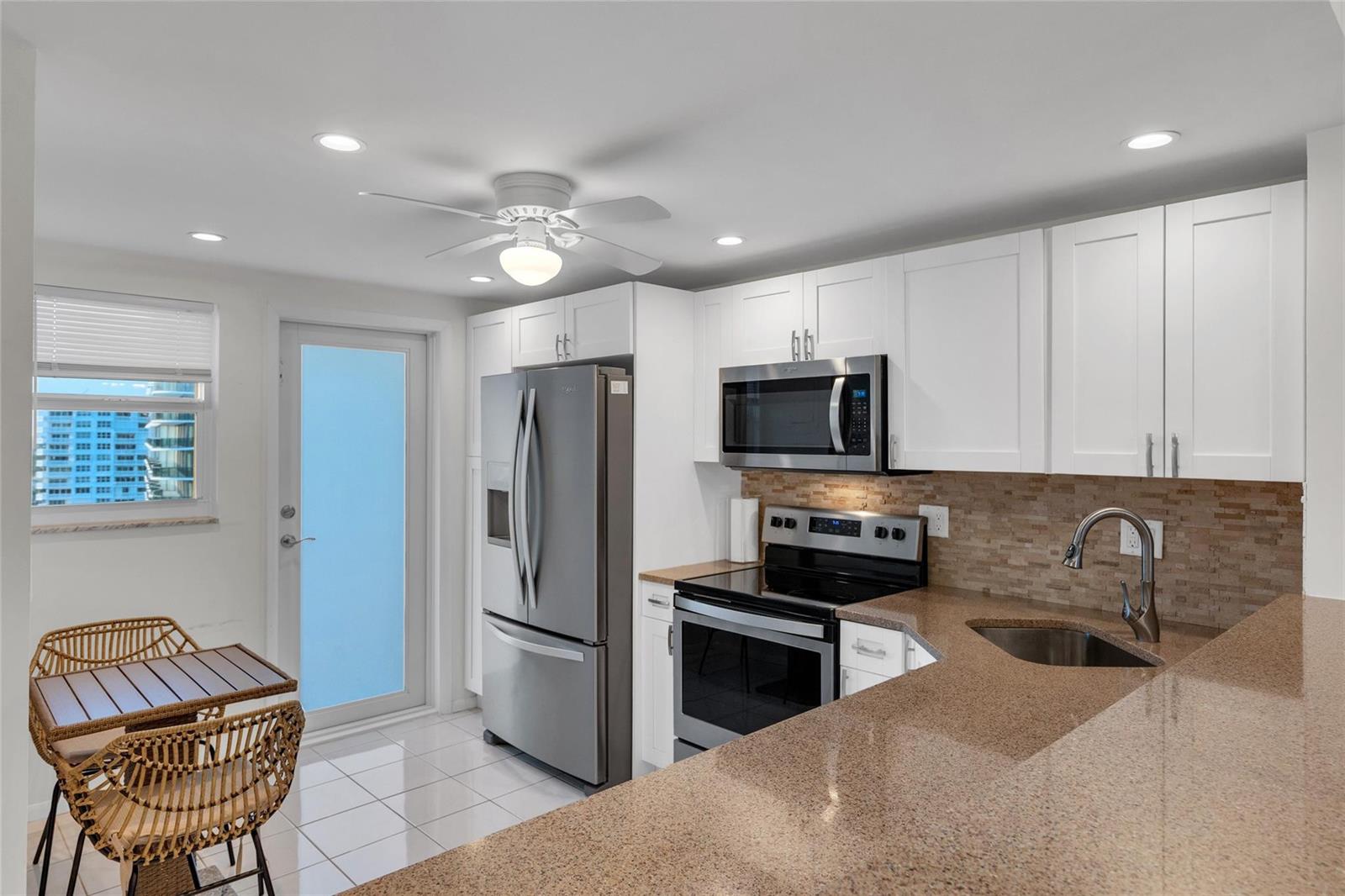 A kitchen features white cabinets, stainless steel appliances, granite countertops, and a small dining area — 750 N Ocean Boulevard # 1503, Pompano Beach FL 33062, POMPANO BEACH, FL
