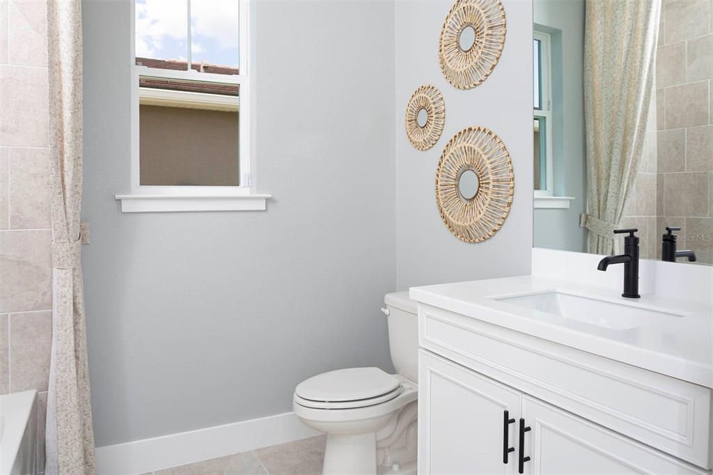 A bathroom features a white vanity with a black faucet, a toilet, and wall decor — 17760 STILLNESS COURT, VENICE, FL