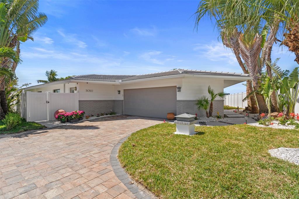 A single-story house with a paved driveway, a two-car garage, and tropical landscaping — 11050 7TH STREET E, TREASURE ISLAND, FL