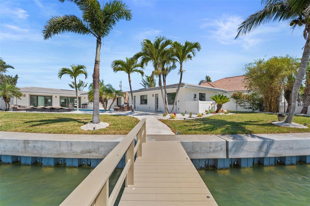 A wooden dock leads to a white house with a pool and palm trees — 11050 7TH STREET E, TREASURE ISLAND, FL