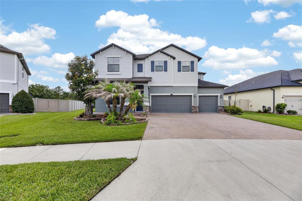 A two-story suburban house features a gray exterior, a three-car garage, and a paved driveway — 2905 HILLIARD DRIVE, WESLEY CHAPEL, FL