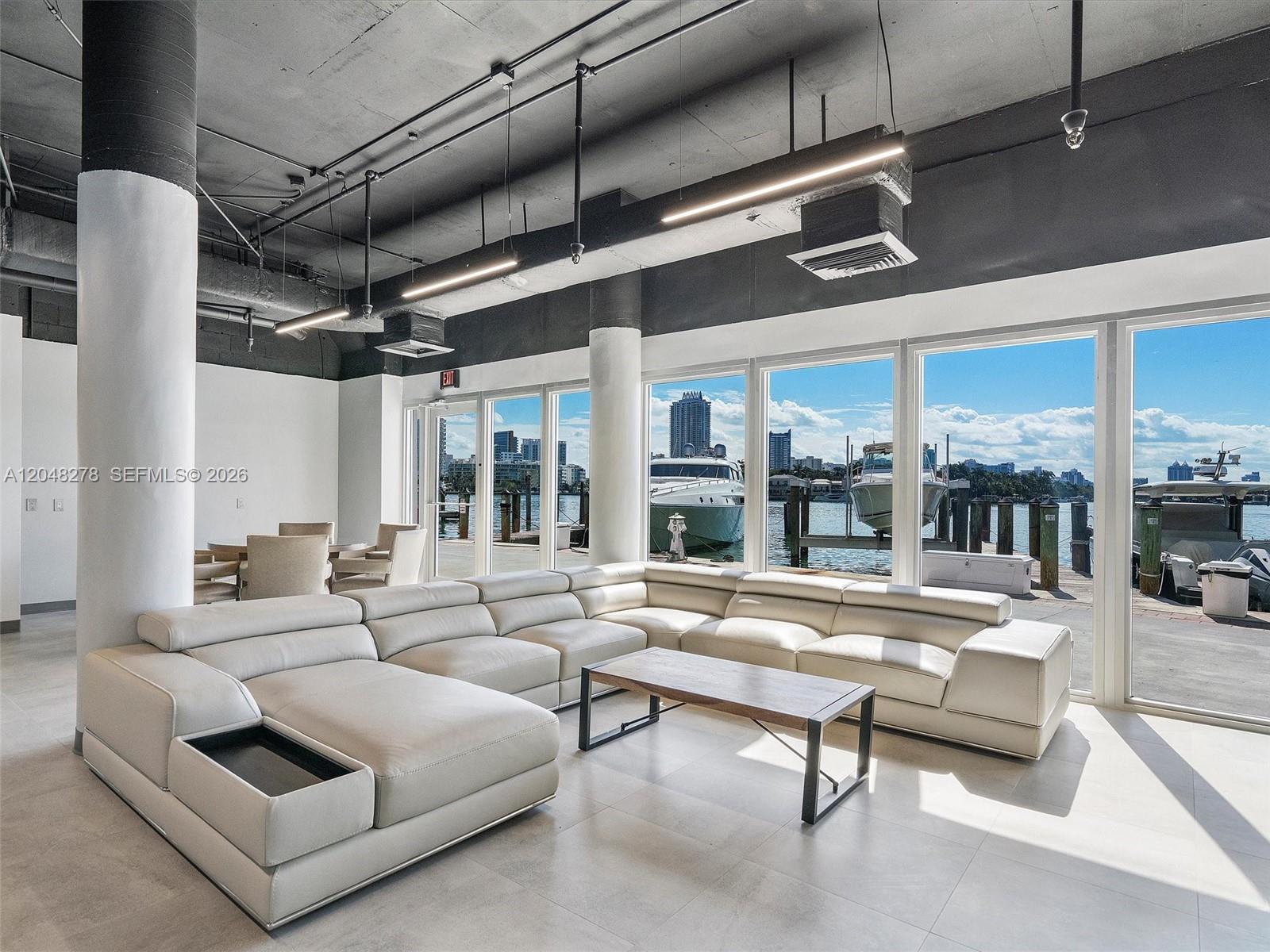 A modern living room features a large white sectional sofa, concrete ceilings, and waterfront views — 900 SW Bay Dr, Miami Beach FL 33141, MIAMI BEACH, FL