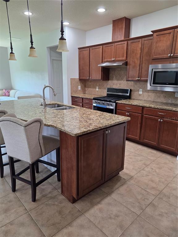 A kitchen features wood cabinets, granite countertops, a center island, and three pendant lights — 576 CANTABRIA DRIVE, DAVENPORT, FL