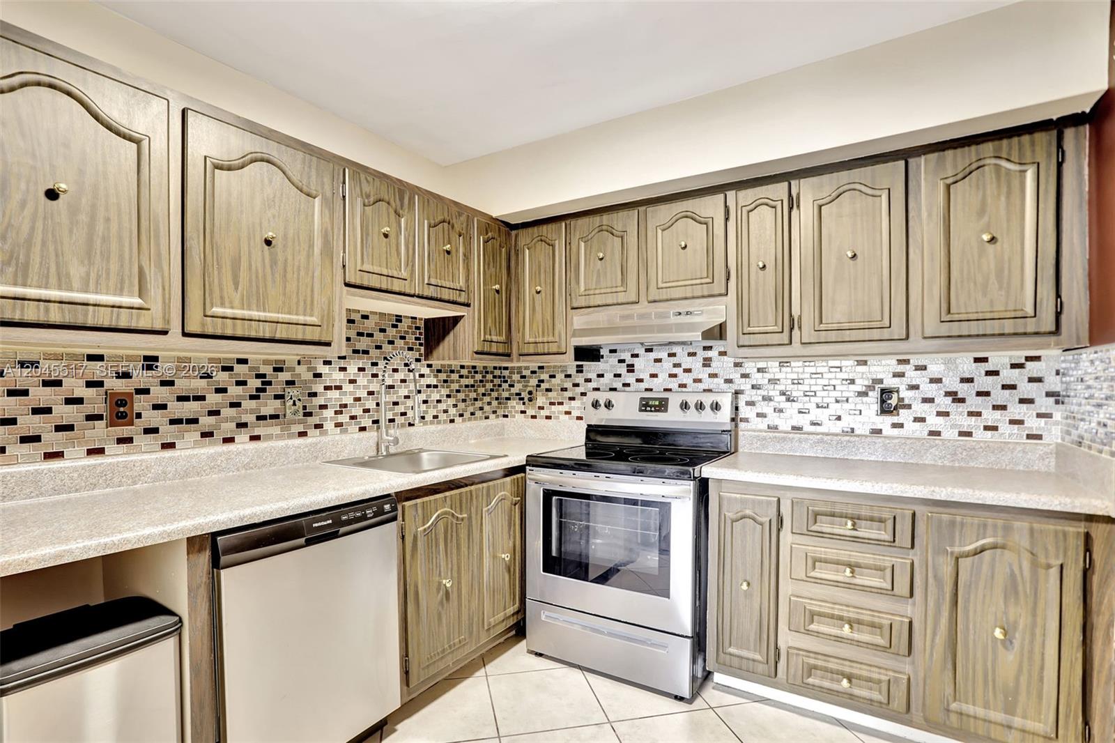 A kitchen features wood-grain cabinets, stainless steel appliances, and a multi-colored mosaic tile backsplash — 470 N Laurel Dr # 1A, Margate FL 33063, MARGATE, FL