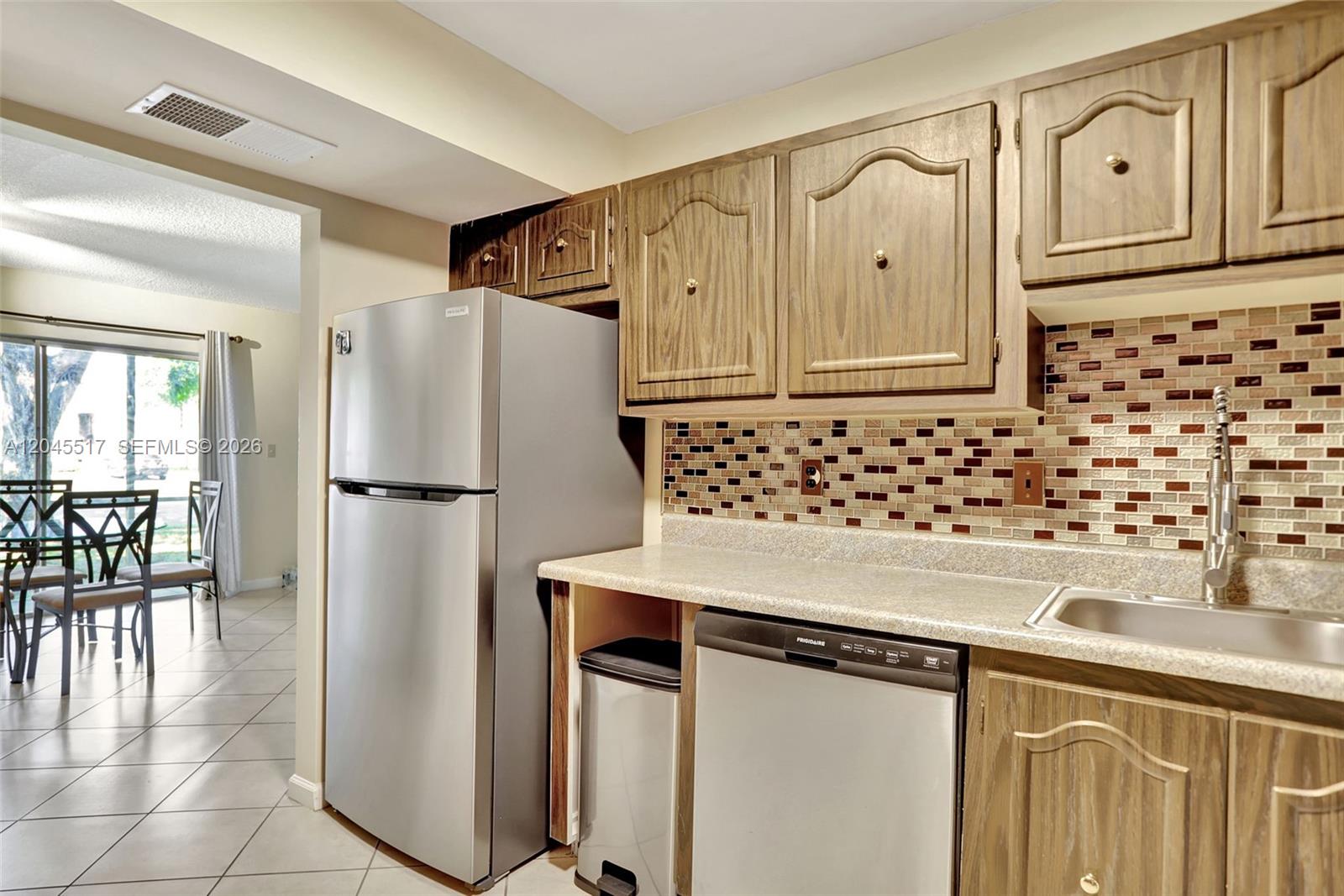 A kitchen features wood cabinets, stainless steel appliances, a mosaic backsplash, and a tile floor — 470 N Laurel Dr # 1A, Margate FL 33063, MARGATE, FL