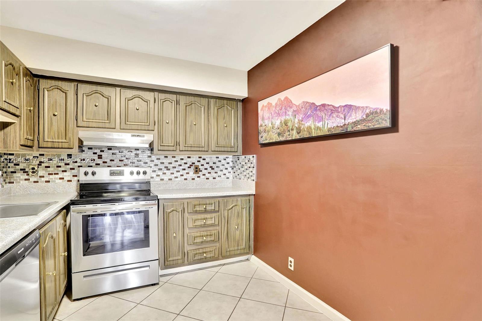 A kitchen features wood cabinets, a stainless steel stove, tiled backsplash, and a wall painting — 470 N Laurel Dr # 1A, Margate FL 33063, MARGATE, FL