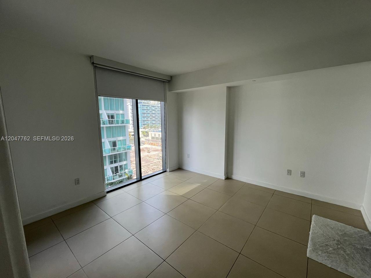 A bright, empty room with large floor tiles, white walls, and a sliding glass door — 31 SE 6th St # 1004, Miami FL 33131, MIAMI, FL