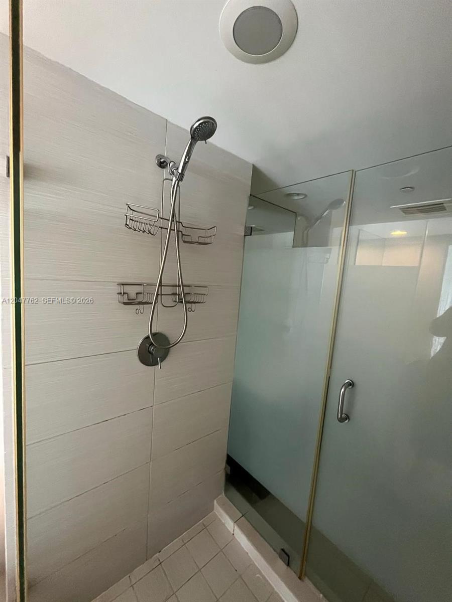 A walk-in shower features light-colored horizontal wall tiles, a handheld showerhead, and glass doors — 31 SE 6th St # 1004, Miami FL 33131, MIAMI, FL