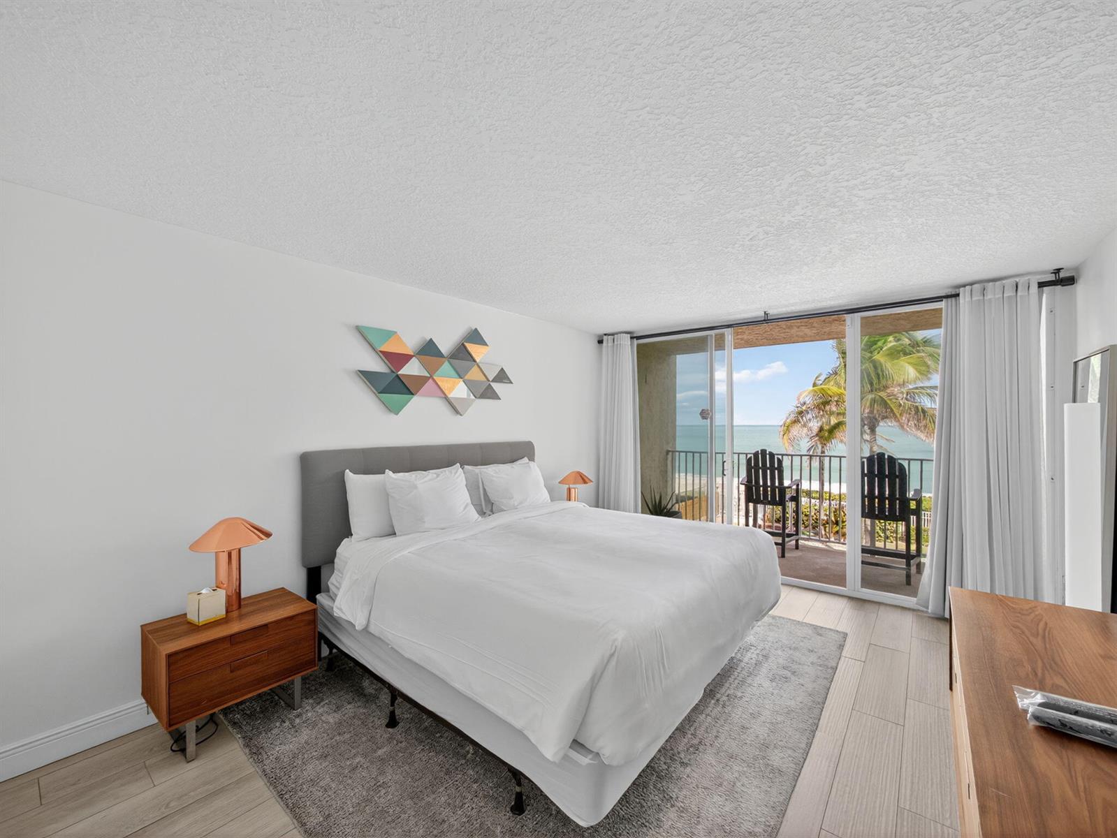 A bedroom with a bed, modern decor, and a balcony overlooking the ocean — 9800 S Ocean Drive # 302, Jensen Beach FL 34957, JENSEN BEACH, FL