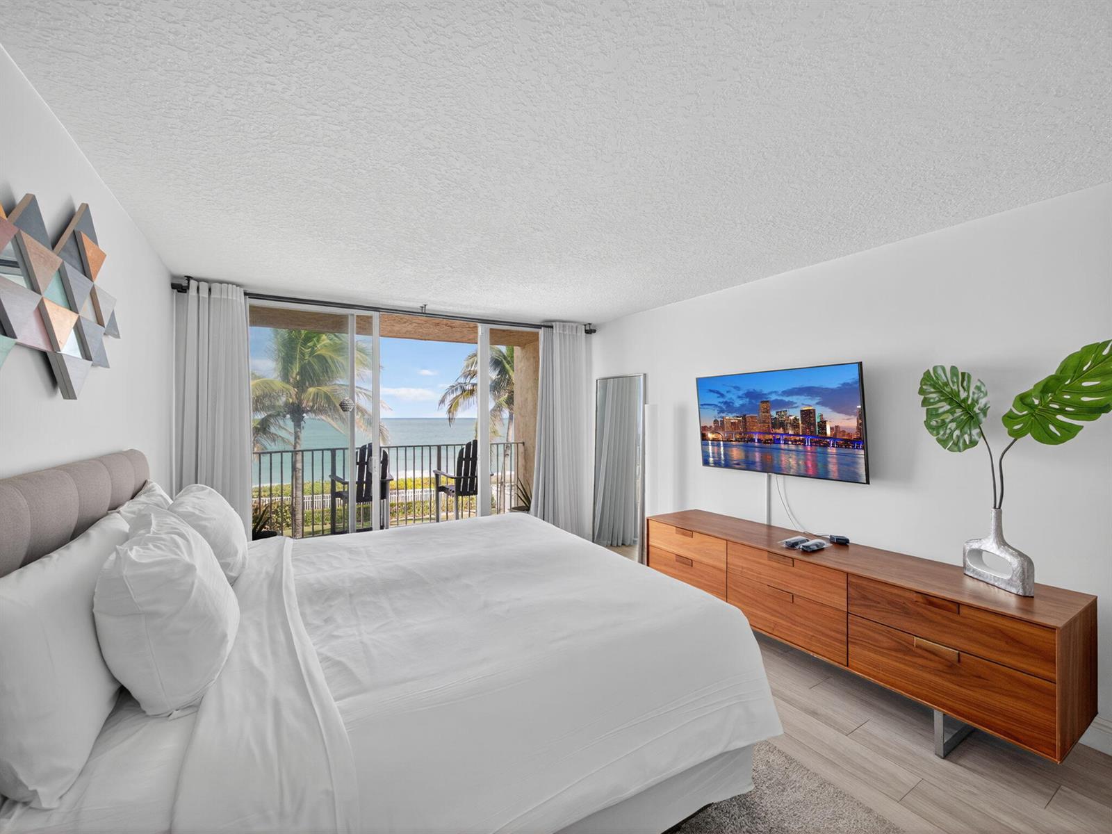 A bedroom with a king bed, wooden dresser, wall-mounted television, and a balcony overlooking the ocean — 9800 S Ocean Drive # 302, Jensen Beach FL 34957, JENSEN BEACH, FL