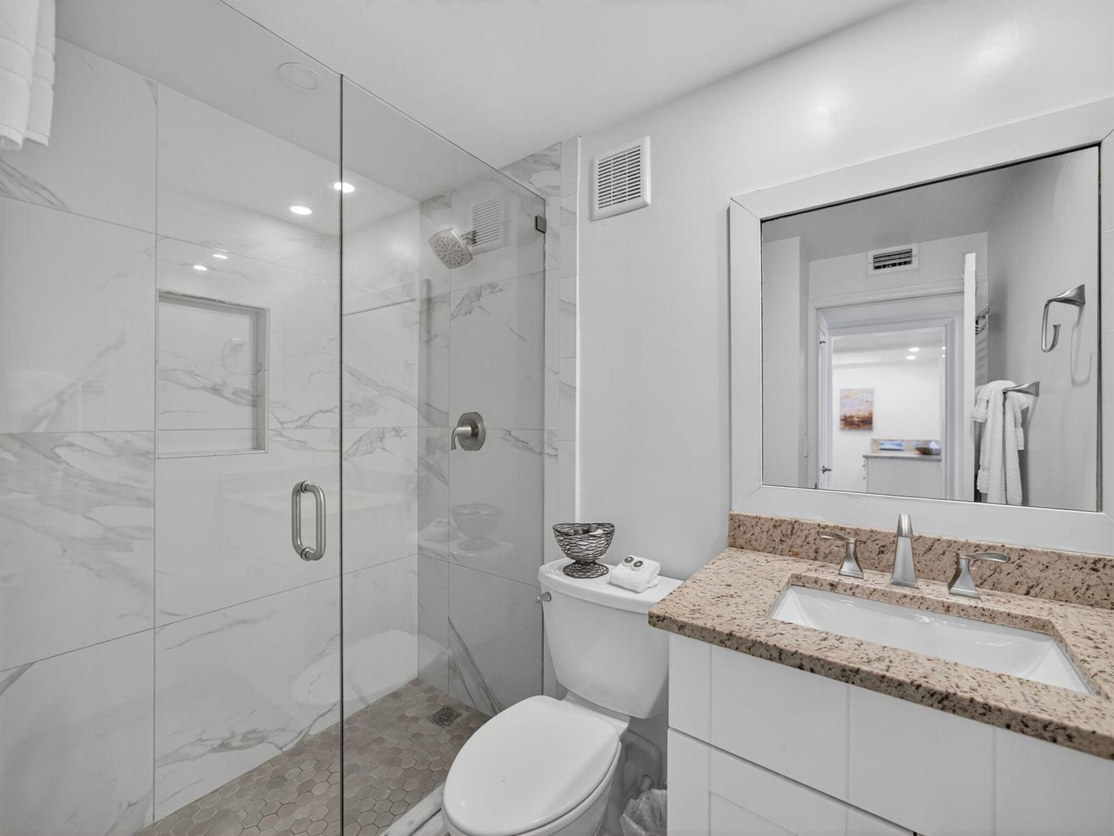 A bathroom features a glass-enclosed marble shower, a white vanity with granite countertop, and toilet — 9800 S Ocean Drive # 302, Jensen Beach FL 34957, JENSEN BEACH, FL