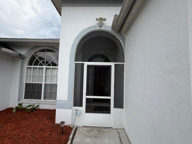 A white stucco house exterior features an arched entryway with a screen door — 6213 ASHFIELD PLACE, WESLEY CHAPEL, FL