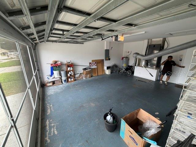 An interior view of a garage with a concrete floor, storage items, and a person — 6213 ASHFIELD PLACE, WESLEY CHAPEL, FL