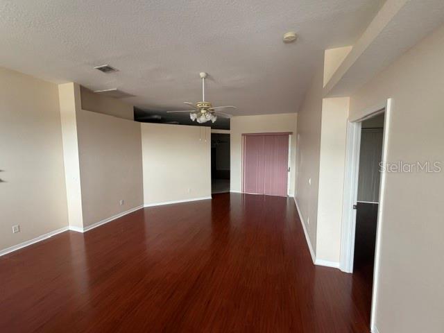 An empty room features dark wood-look flooring, beige walls, and a ceiling fan — 6213 ASHFIELD PLACE, WESLEY CHAPEL, FL