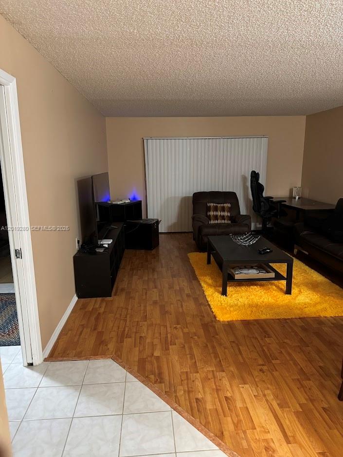 A living room features wood-look flooring, a yellow area rug, and a sliding glass door — 4602 Martinique Way # A2, Coconut Creek FL 33066, COCONUT CREEK, FL