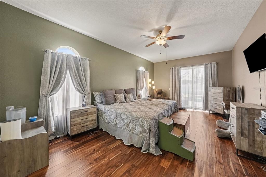 A bedroom features wood-look flooring, a ceiling fan, a king bed, and sliding glass doors — 18425 EASTWYCK DR, TAMPA, FL