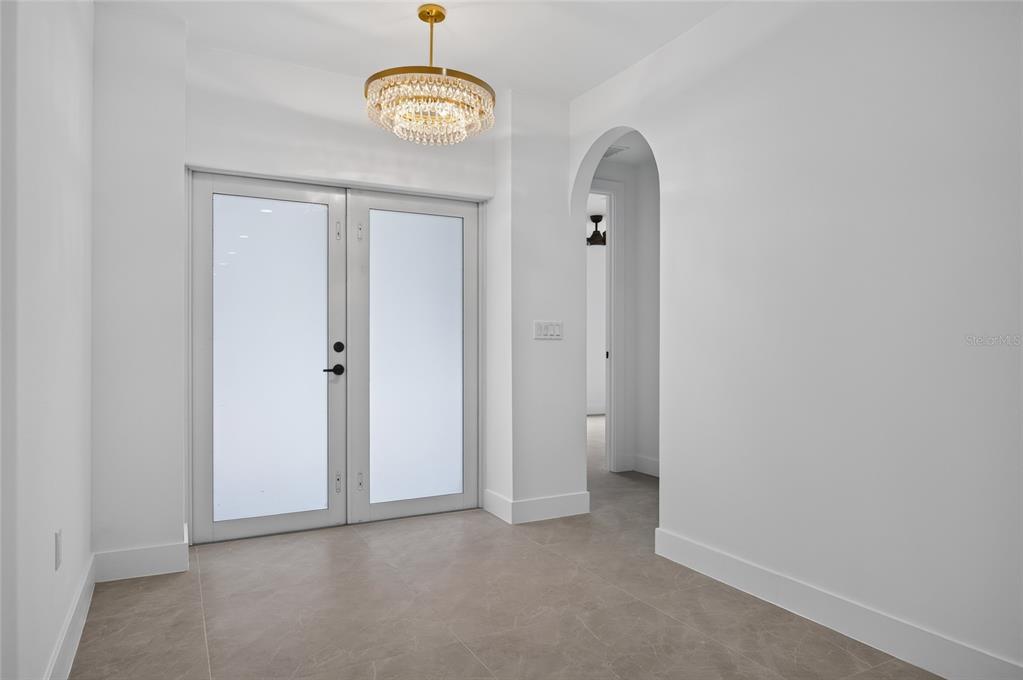 A bright entryway features a crystal chandelier, double glass doors, and light-colored tile flooring — 1177 COMMERCE STREET, PORT CHARLOTTE, FL