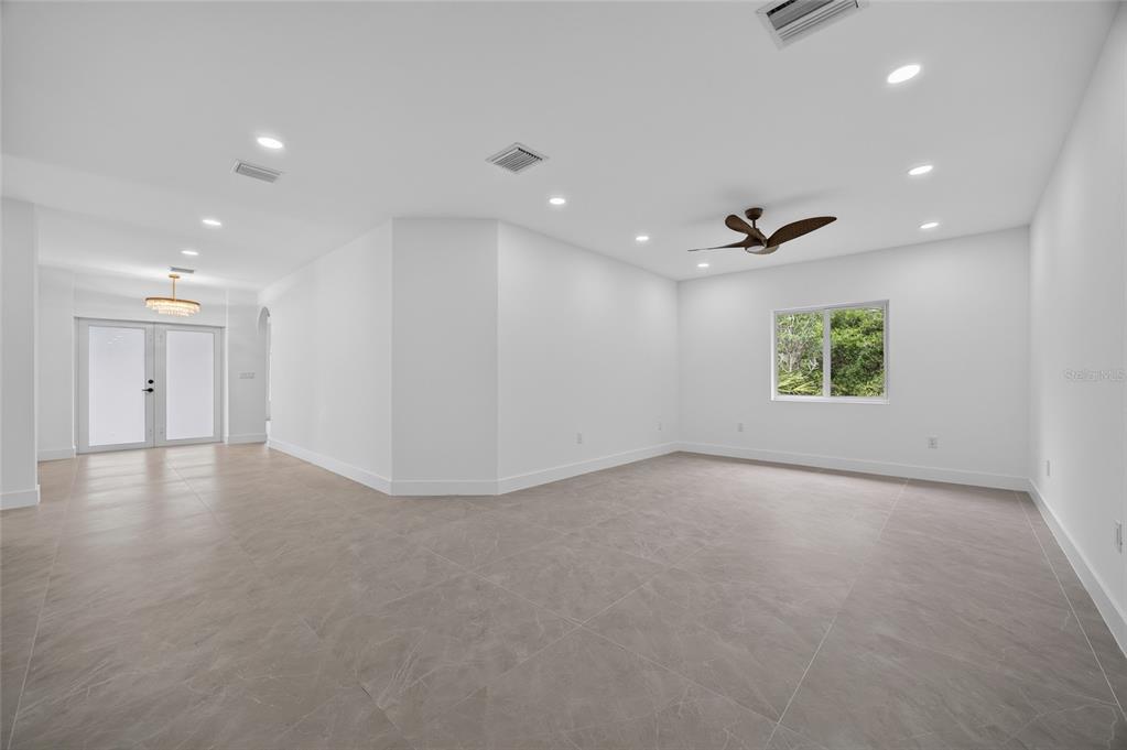 A spacious, white-walled room with large gray floor tiles, a ceiling fan, and a window — 1177 COMMERCE STREET, PORT CHARLOTTE, FL