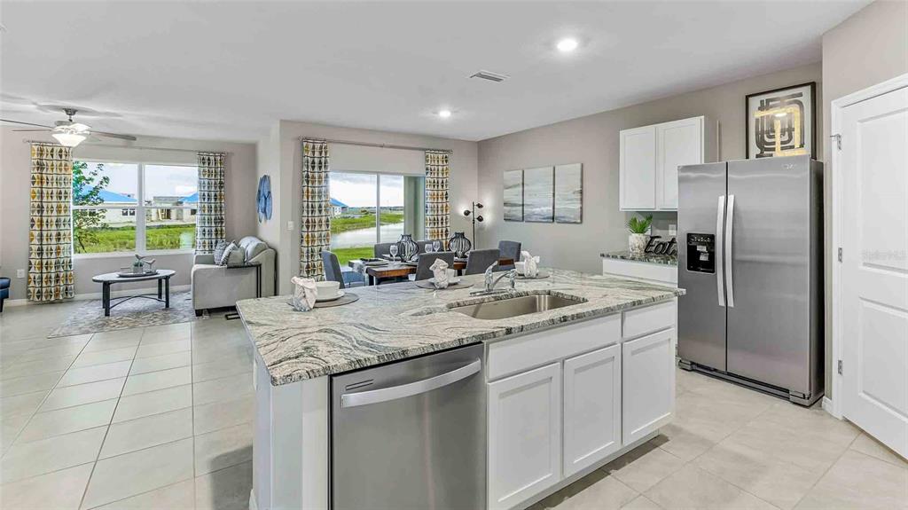 A kitchen with a granite-topped island and stainless steel appliances overlooks a dining and living area — 10840 QUAIL GROVE WAY, SAN ANTONIO, FL