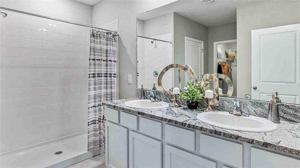 A bathroom features a double vanity with granite countertops, white cabinets, and a shower-tub combo — 10840 QUAIL GROVE WAY, SAN ANTONIO, FL